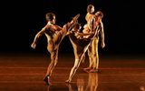 Two dancers kick one leg in the air whilst in the background a male dancer lifts a female.