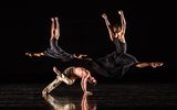 Two people leap in the air whilst a third dancer contorts their body on the floor.