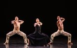 Three dancers bend their knees and stretch one arm forwards.