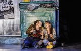 Two females sit on the floor in front of a bin smoking and drinking.