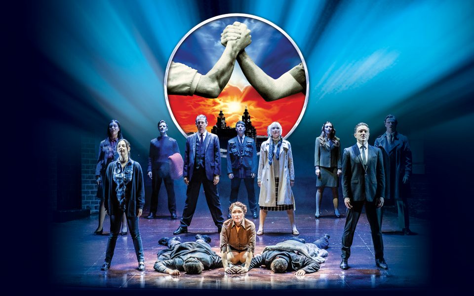Two men lay face down on the ground. A woman kneels between them and others stand around them.