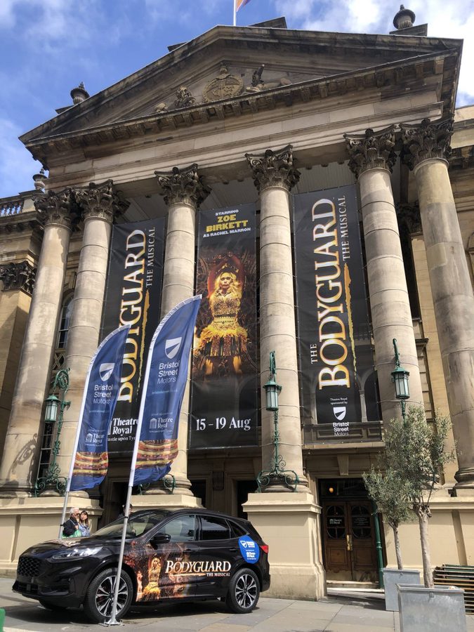 The outside of Newcastle Theatre Royal, with banners for The Bodyguard and a car with The Bodyguard branding.