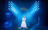 One female stands on a dimly lit stage.