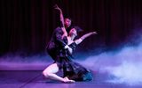 A pair of dancers work together. There is smoke around them and a black back drop.