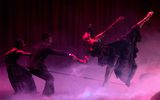 A female balances on one leg whilst she kicks the other behind her. The bottom of the stage is filled with smoke and it is dimly lit.