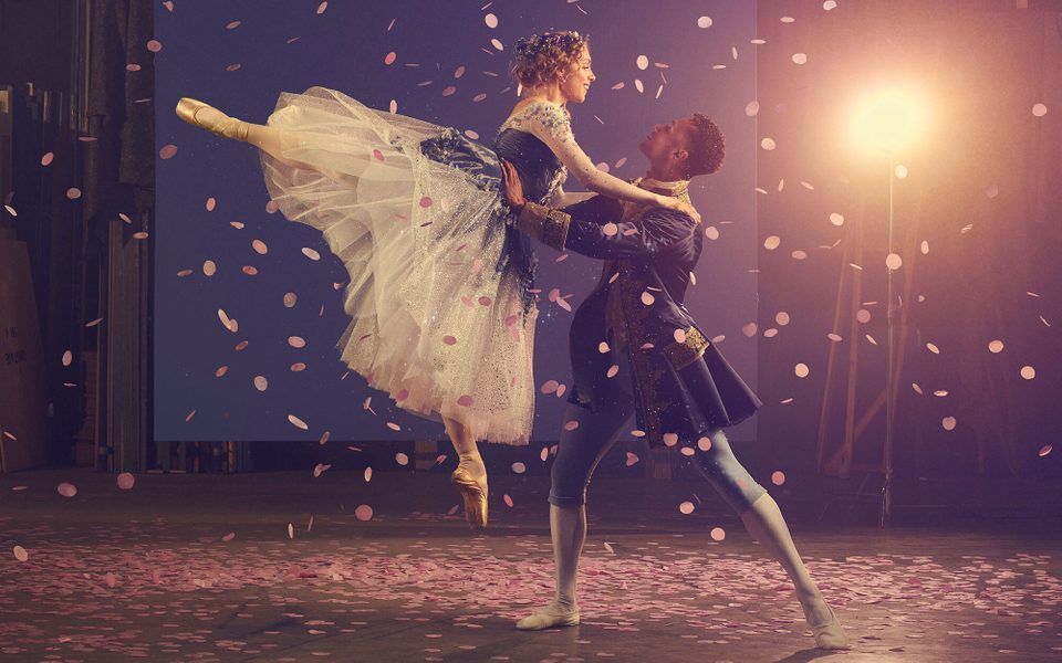 A man holds a woman wearing a glittery dress with a tutu up in the air.
