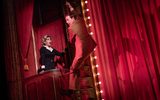 A female looks shocked as a male climbs out of the theatre box using a rope.