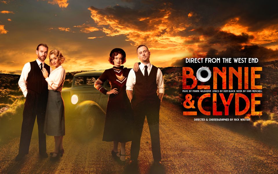 two male and female couples dressed in 1930's clothes stand in front of a car and sunset.