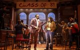 Two people talk in the foreground whilst people in the background talk and dance in front of a banner reading 'Class of '89'