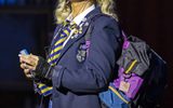 A young female wearing a school uniform and carrying a backpack listens to music using a walkman.