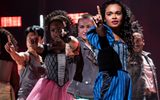 A group of cast members standing with their arms outstretched and a finger in the air.