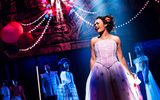 A female wearing a ball gown singing whilst people in the background look at her.