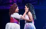 A two females wearing ball gowns looking at each other, smiling.