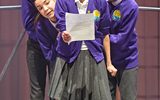 Four people crowd around a piece of paper and look apprehensively at it.