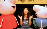 A young female sitting on the floor next to Peppa and George and some other puppet creatures.