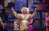 A woman wearing a golden outfit sings with her arms in the air.