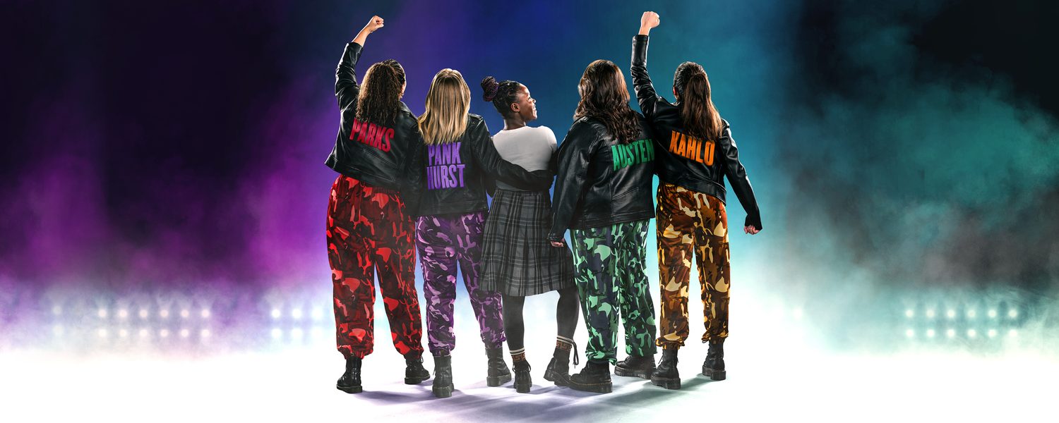 5 women from the back. 4 in leather jackets and camp trousers and one in a tartan skirt. 2 hold fists in the air.