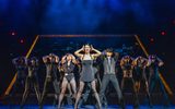 A group of dancers, dressed all in black with their hands by their heads.