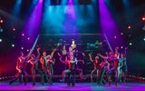 A group of dancers raise one female in the air, they all have a shocked look on their faces.