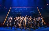 A group of dancers facing the audience leaning backwards with their hands to their foreheads.