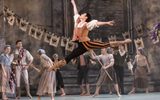 A male dancer leaps high in the air whilst other characters watch them in awe.