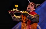 A male character with two animal horns on their head holds a book in front of them with a yellow flower growing out of it.