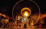 A huge lion puppet dominates the stage. There is an orange glow.