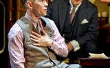 A male talking. He is wearing a grey waistcoat, a pink shirt and has short brown hair.