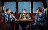 Three males laugh and smile at each other, they are sitting around a table.