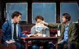 Three males sit around a table and one holds a poster reading 'JAWS'.