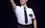 A male in a suit stretches his arm in the air whilst holding a Book of Mormon in the air.