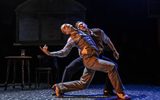 Two males dance together. They are wearing grey suits.