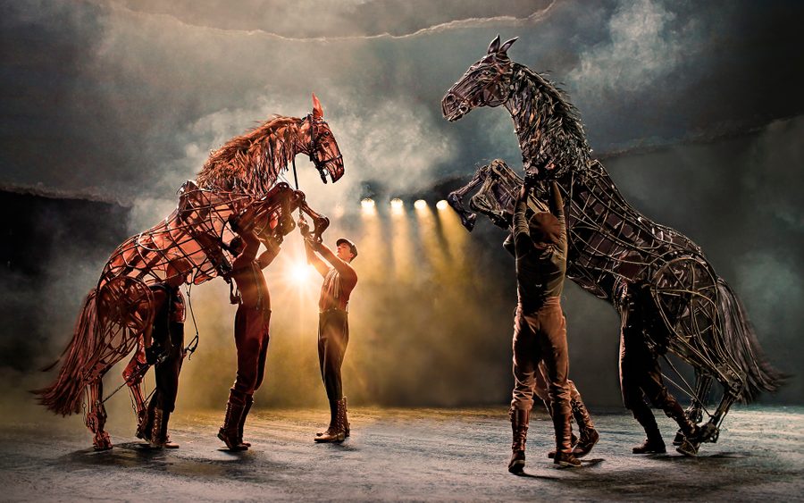 War Horse Men in First World War costumes attend to two horses depicted by brown puppets with stage spotlights behind