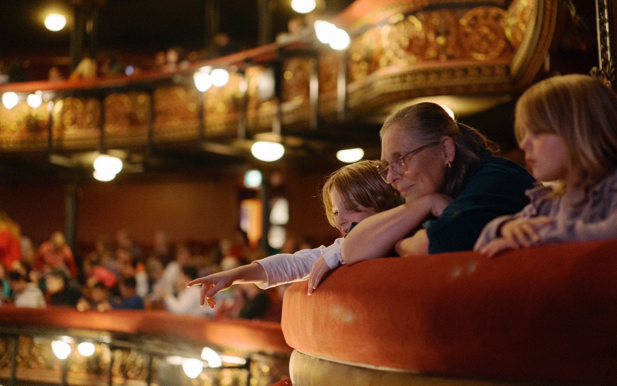 A mana and a child peep over an ornate balustrade looking down in awe at the stage where opera plays